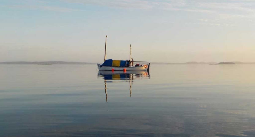 A sailboat floats on calm water, reflecting the gentle colors of the sky.